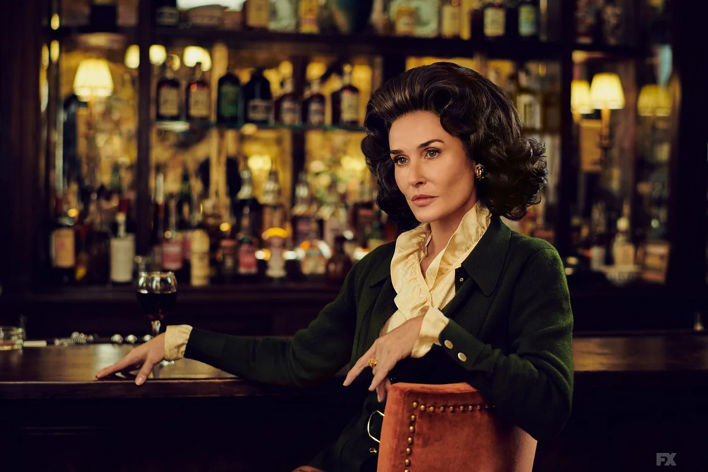 Demi Moore as Ann Woodward sitting at a bar in a studded bar stool, wearing a dark green cardigan and white blouse. Demi Moore as Ann Woodward sitting at a bar in a studded bar stool, wearing a dark green cardigan and white blouse.